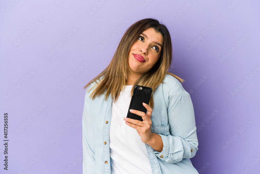 Young indian woman holding a phone isolated dreaming of achieving goals and purposes Young indian woman holding a phone isolated dreaming of achieving goals and purposes