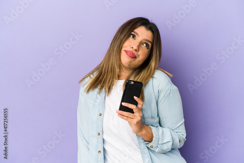 Young indian woman holding a phone isolated dreaming of achieving goals and purposes