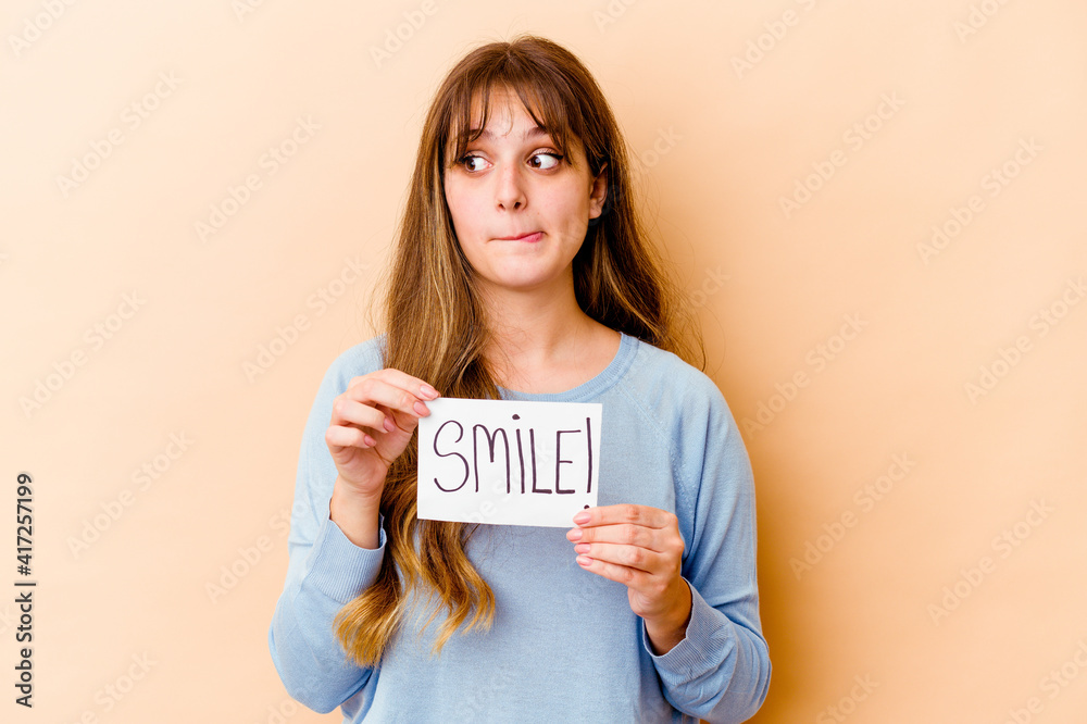 Young caucasian woman holding a Smile placard isolated confused, feels doubtful and unsure. Young caucasian woman holding a Smile placard isolated confused, feels doubtful and unsure.