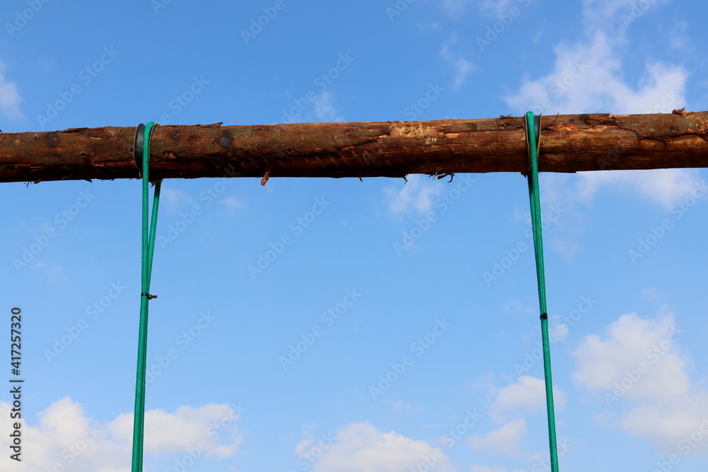 Two green ropes fixed in a wooden beam against a blue sky background Two green ropes fixed in a wooden beam against a blue sky background