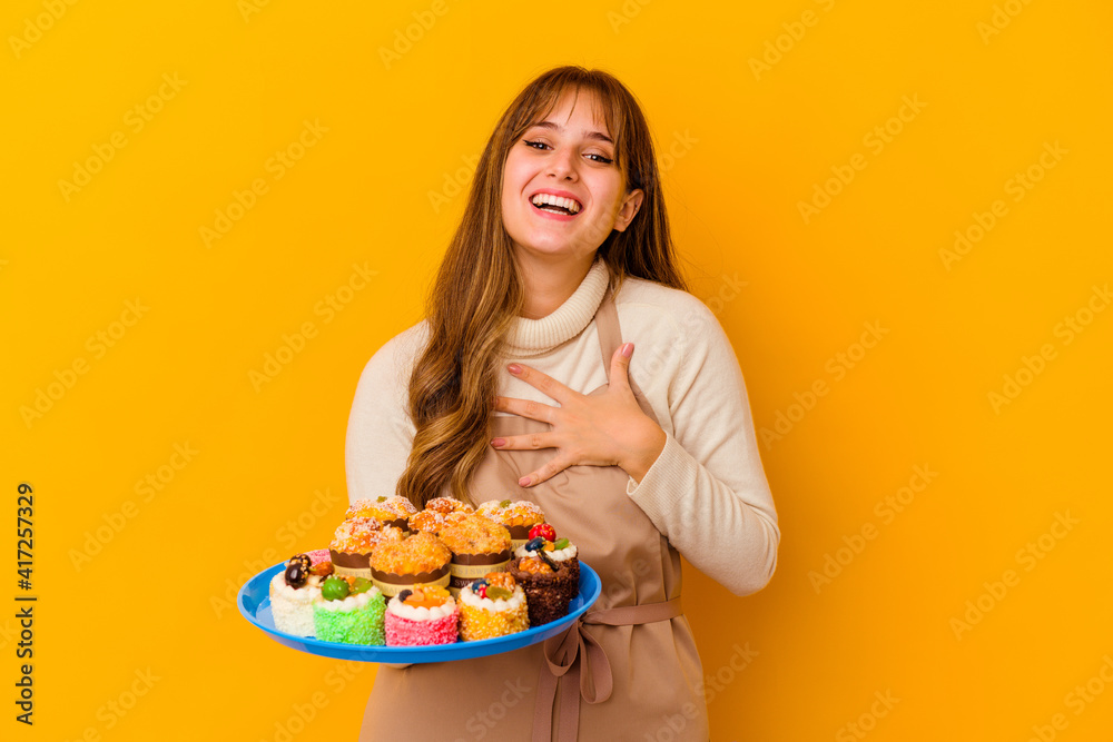 Young pastry chef woman isolated on yellow background laughs out loudly keeping hand on chest.