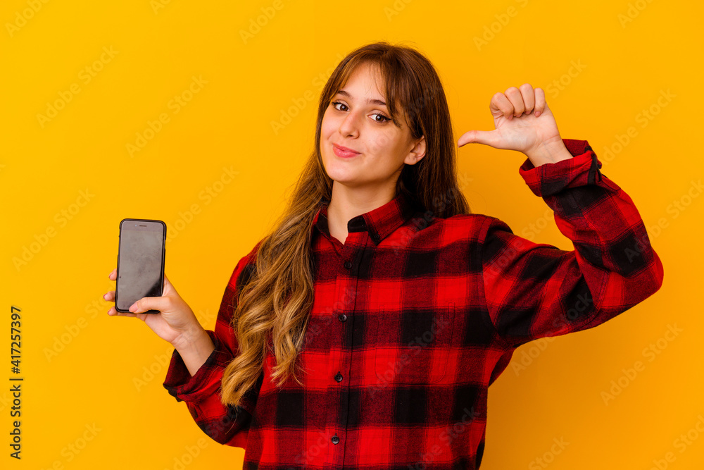 Young caucasian woman holding phone isolated on yellow background feels proud and self confident, example to follow. Young caucasian woman holding phone isolated on yellow background feels proud and self confident, example to follow.