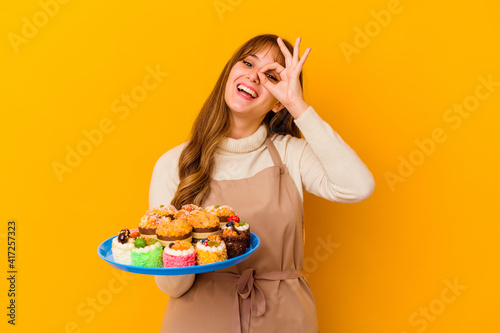 Young pastry chef woman isolated on yellow background excited keeping ok gesture on eye.