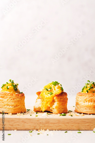 Three Vol-au-Vent filled with cauliflower and saffron sauce, lined on a wooden cutting board and sprinkled with cheese and chive. photo