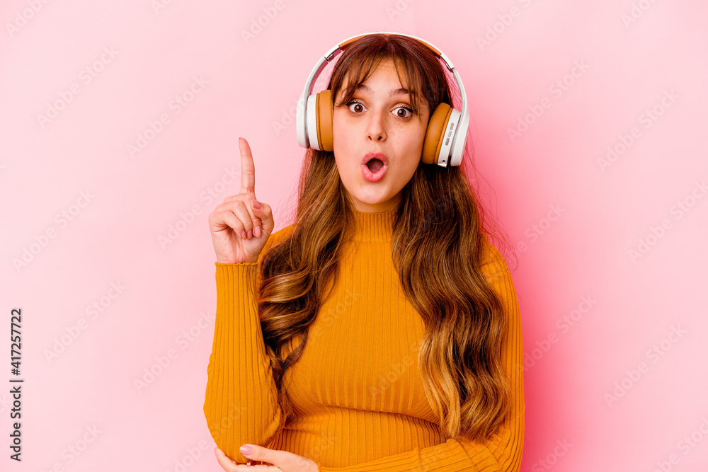Fototapeta premium Young caucasian woman listening music with headphones isolated having some great idea, concept of creativity.