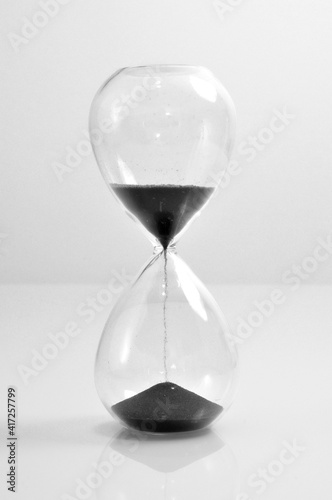 Hourglass transparent crystal black sand falling down vertical old vintage clock isolated on white background 