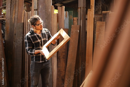 Young Caucasian carpenter man is making wooden frame in his own garage style workshop for hobby with copy space