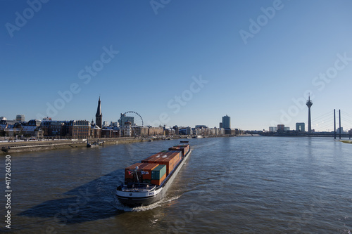 Outdoor sunny view with container ship on Rhine River and background of Düsseldorf cityscape, Germany. 