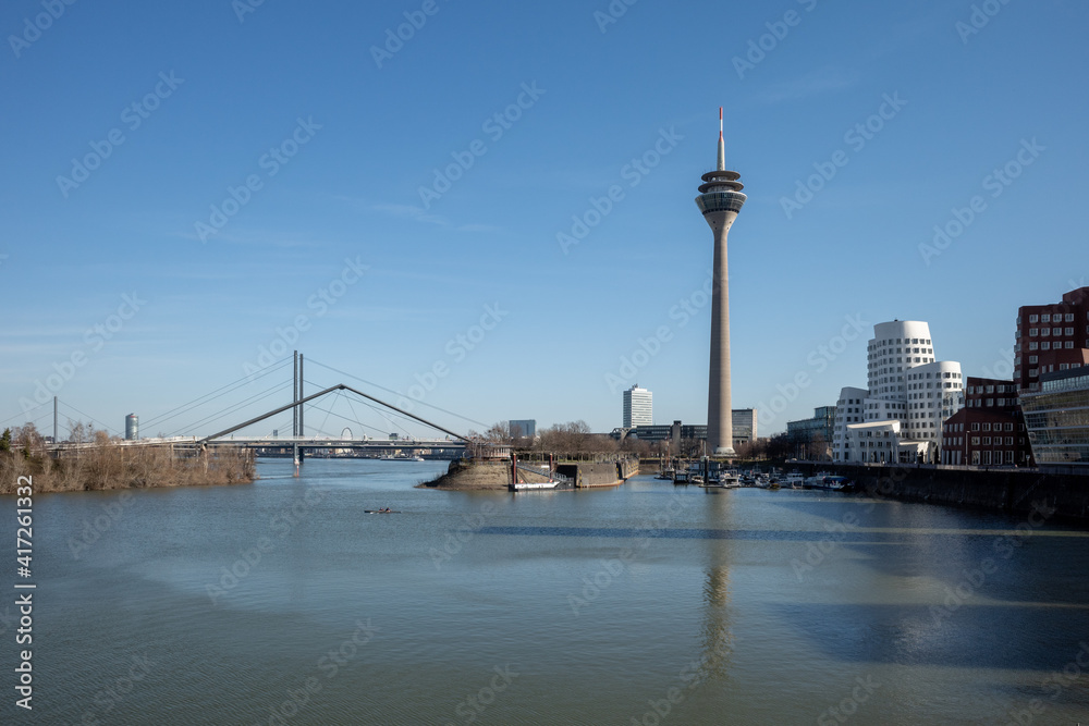 Outdoor sunny view of harbour, pier, pedestrian bridge, Rhein tower and promenade on riverside of Rhein River and cityscape at media harbour, in Düsseldorf, Germany,