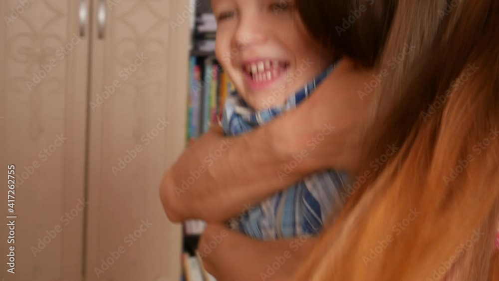 A young woman hugs from behind a little boy and they smile and laugh close-up A young woman hugs from behind a little boy and they smile and laugh close-up