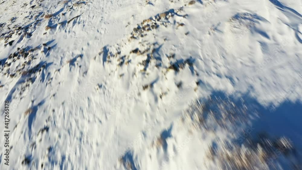 Dynamic aerial view of man in showshoes and with trekking poles walking on snow uphill on sunny winter day, action drone shot Dynamic aerial view of man in showshoes and with trekking poles walking on snow uphill on sunny winter day, action drone shot