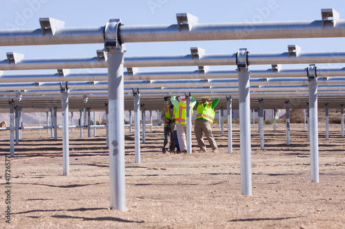 workers on construction site standing under metal tubing grid at solar farm installing solar panels photo
