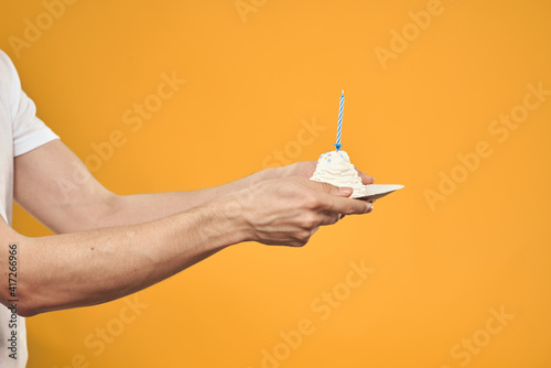 Cake with a candle in a man's hand on a yellow background cropped view Copy Space