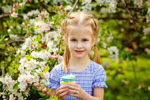 A child in a blooming apple orchard enjoys a warm spring day. The girl holds a cake in her hands, wants to eat it.