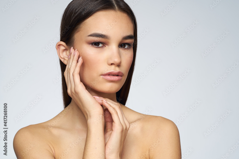 Woman with long hair bared shoulders clean skin body care light background