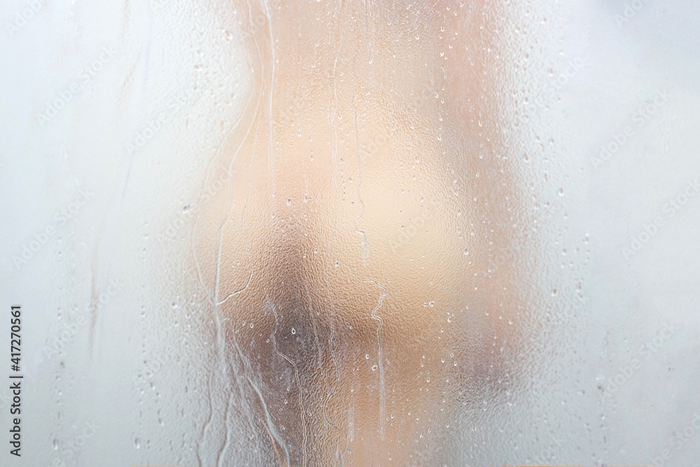A sexy woman's buttock is behind the mirror. She is showering a drop of water on her ass.