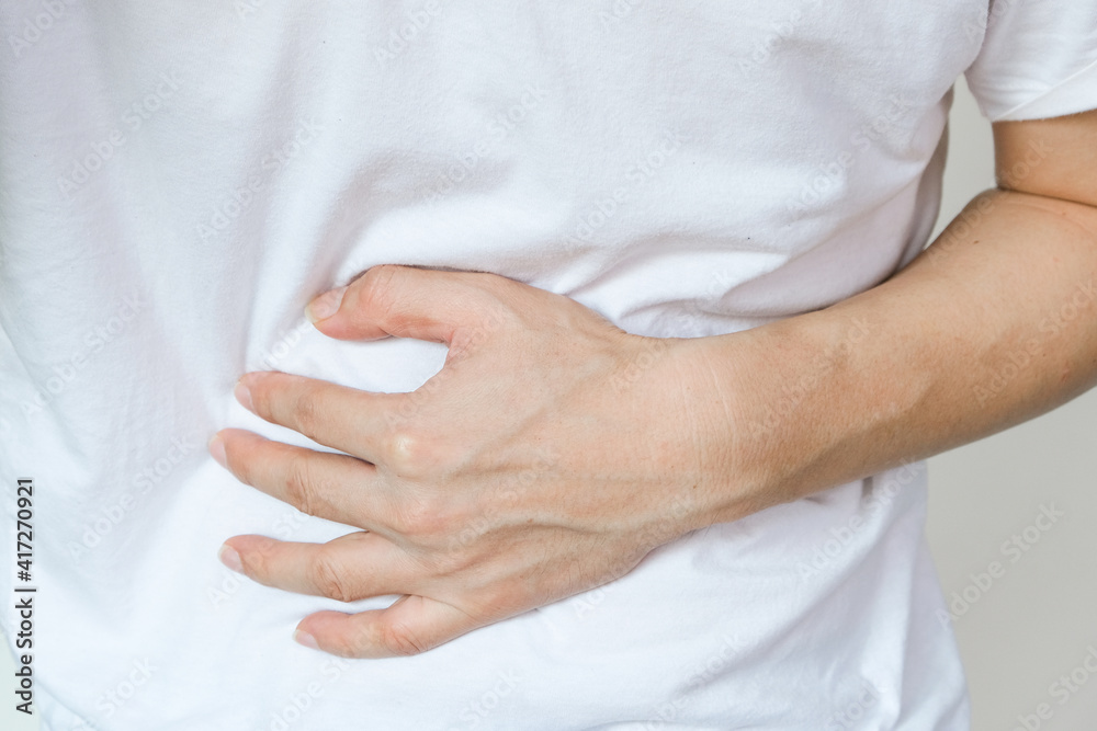 Young man uses his hands to hold his stomach and has a severe stomachache.on isolated white background Young man uses his hands to hold his stomach and has a severe stomachache.on isolated white background