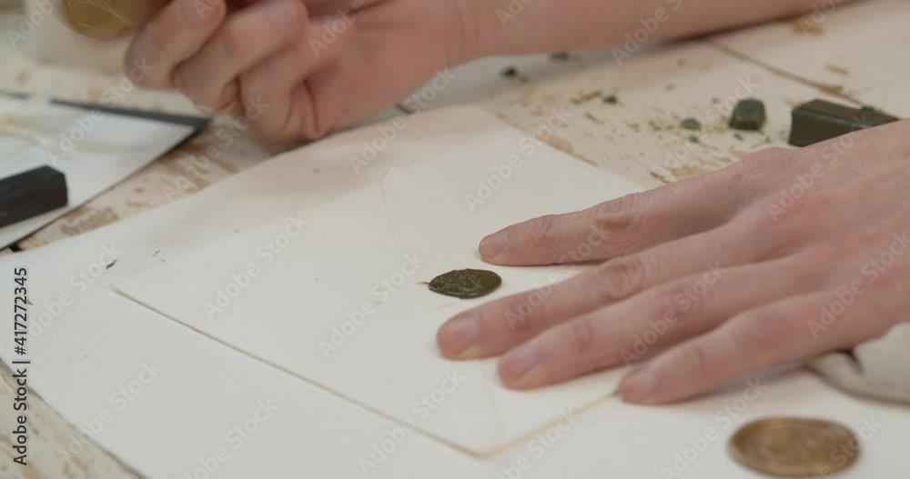 An artisan pressing a stamp over hot wax on the edge of an envelope, in order to seal it (old-style). Handheld shot.
An artisan pressing a stamp over hot wax on the edge of an envelope, in order to seal it (old-style). Handheld shot.