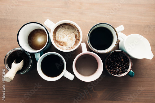 Multiple coffee cups, milk, beans and ground coffee in jar on wooden background