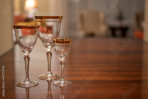 Three empty vintage, gold rimmed wine glasses of various sizes on a table.