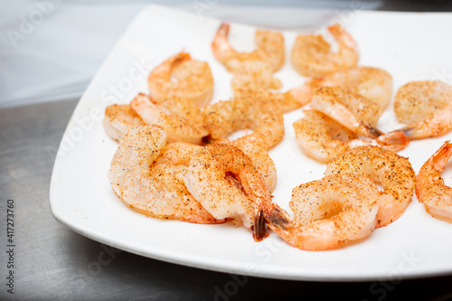 A view of a plate of seasoned raw shrimp, in a restaurant kitchen setting.