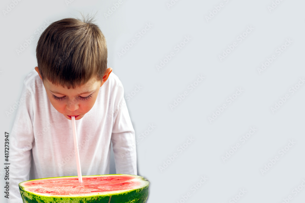A little boy drinks watermelon juice through a straw from half a watermelon. Healthy eating. The concept of proper nutrition, organic and vegetarian food. Copy space for text. A little boy drinks watermelon juice through a straw from half a watermelon. Healthy eating. The concept of proper nutrition, organic and vegetarian food. Copy space for text.