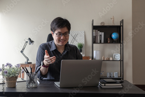 Asian freelancer business man working at home using laptop computer to online video conference chat at workspace desk in living room. Remote work from home. photo