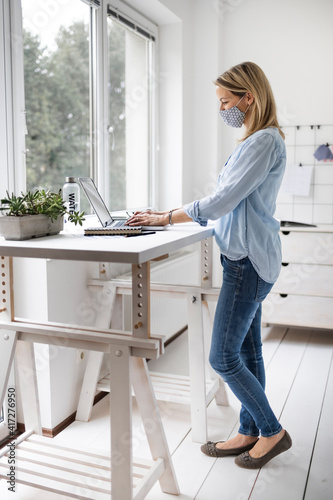 Businesswoman with ffp2 mask working at ergonomic standing workstation in office.