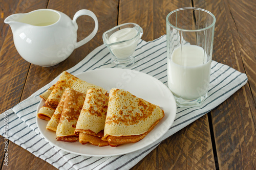 Stack of pancakes or crepes on a plate served with sour cream. Traditional food for the Russian pancake week. Wooden background