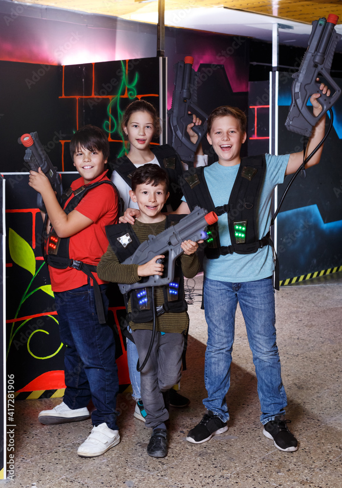Portrait of smiling excited teen boy and girl aiming laser gun at other players during lasertag game in dark room