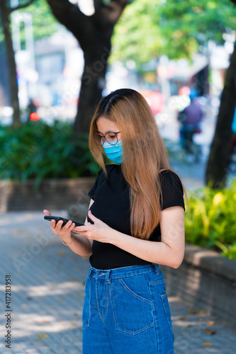 A blonde hair asian girl is using smartphone with a face mask at public during Covid-19