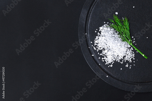 Coarse salt crystals on a black table. Bowl with sea salt. Background for advertising salty.