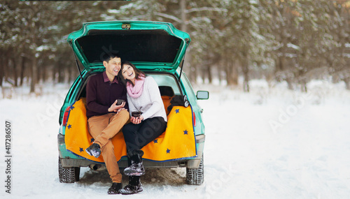 Happy couple sitting in the open trunk of a car in winter on nature