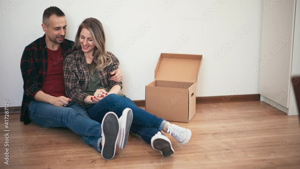 Excited adult couple discussing their new home decoration while sitting on the floor by the white wall in the living room.
