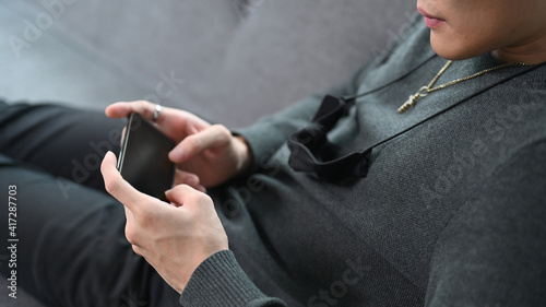 Cropped shot of young man lying on a sofa and holding horizontal smart phone. © Prathankarnpap