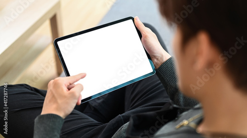 Casual man sitting on a sofa with crossed legs and using digital tablet.