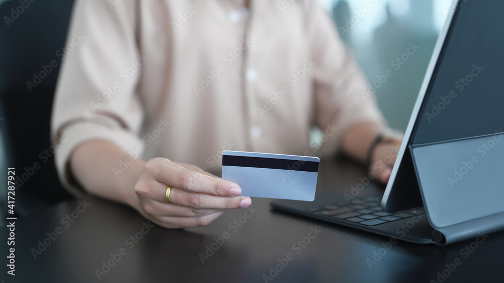Young woman using computer tablet and holding credit card for shopping online or internet banking on blank office desk.