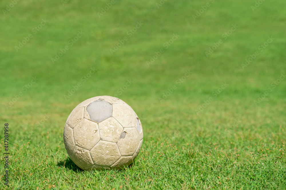 Old soccer ball on green grass of soccer field.