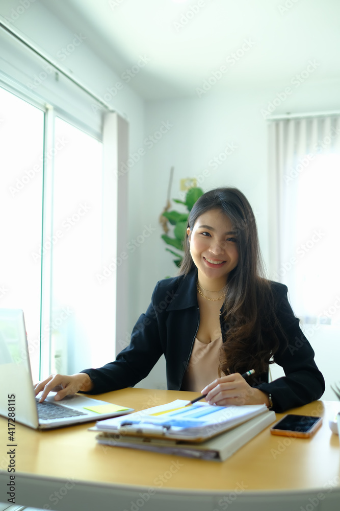 Portrait of cheerful businesswoman in suit working with computer at office desk and smiling to camera. Portrait of cheerful businesswoman in suit working with computer at office desk and smiling to camera.