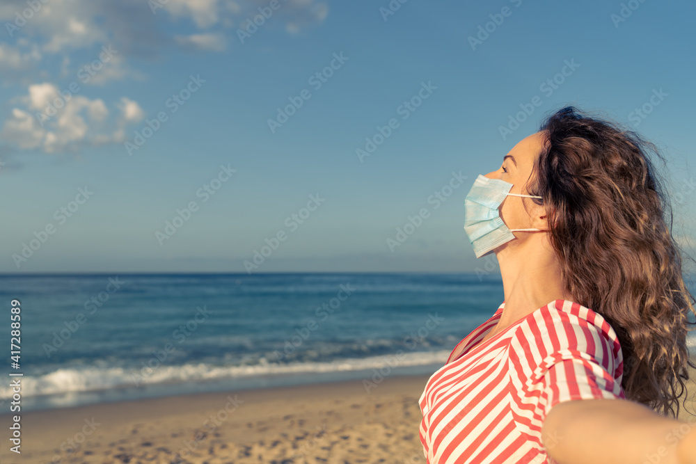 Happy woman wearing medical mask outdoor against blue sea and sky background Happy woman wearing medical mask outdoor against blue sea and sky background