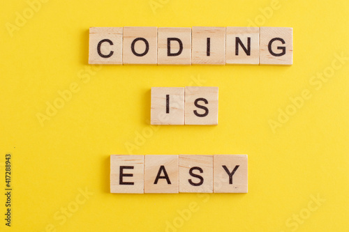 Word Coding is easy made from wooden letters on yellow background. Concept of learning programming languages