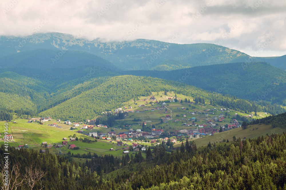 Small mountains village  with meadows rolling through forested hills. Carpathians mountains with beautiful summer weather