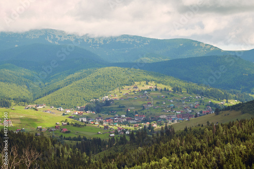 Small mountains village with meadows rolling through forested hills. Carpathians mountains with beautiful summer weather