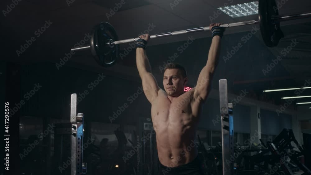 Young powerlifter shirtless doing compound movement in gym. Shoulder press Young powerlifter shirtless doing compound movement in gym. Shoulder press