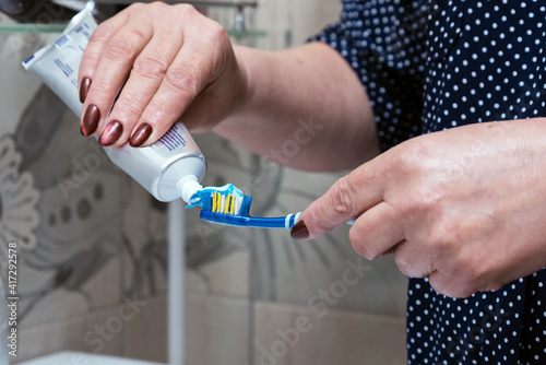 a woman puts toothpaste on a brush before brushing her teeth