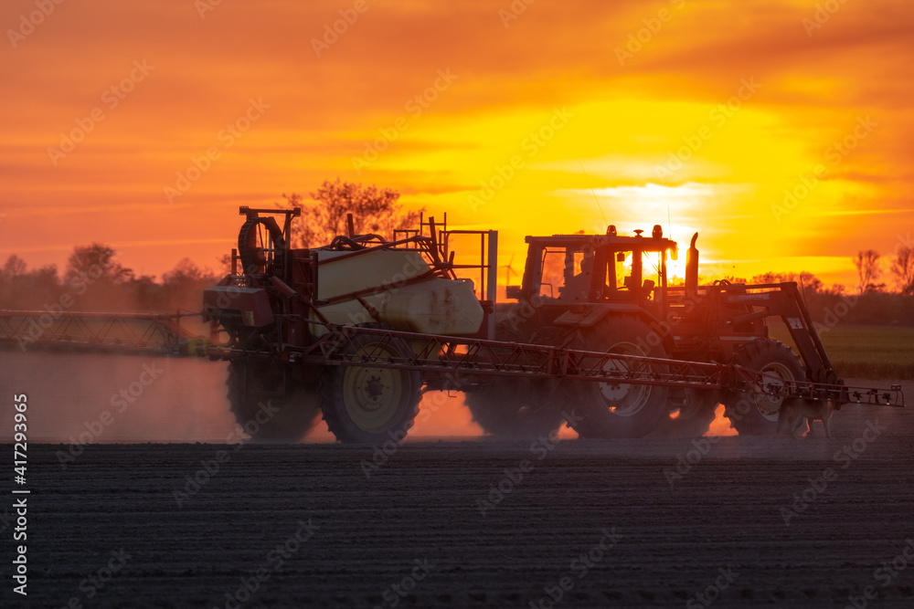 Naklejka premium agricultural tractor with sprayer on the field during sunset