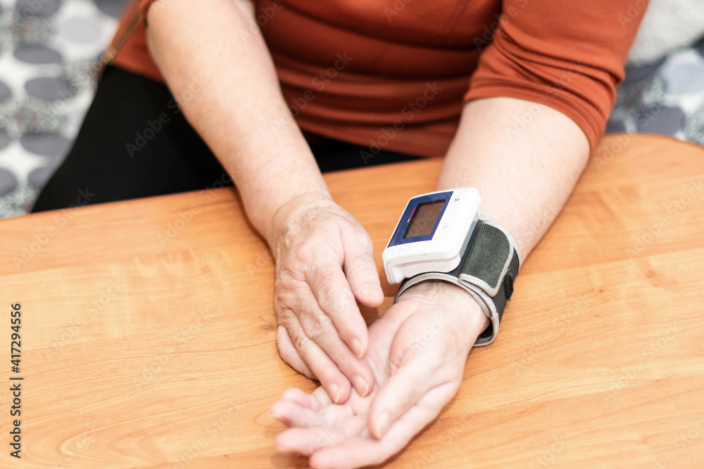 A close-up of an elderly woman's hand. A woman reduces blood pressure with a tonometer on her wrist.