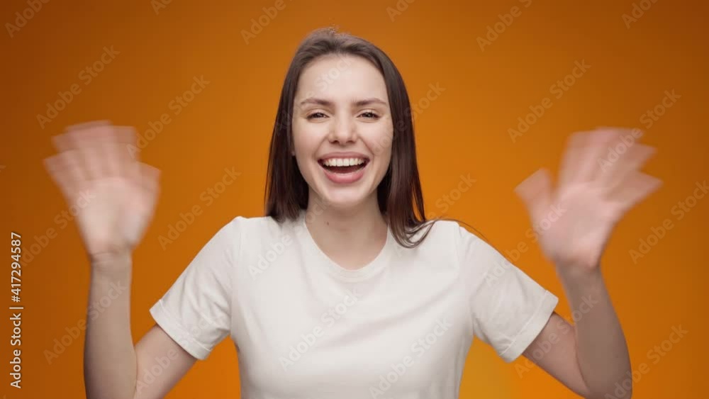 Young woman smiling and shaking hand, greeting someone, against yellow background Young woman smiling and shaking hand, greeting someone, against yellow background