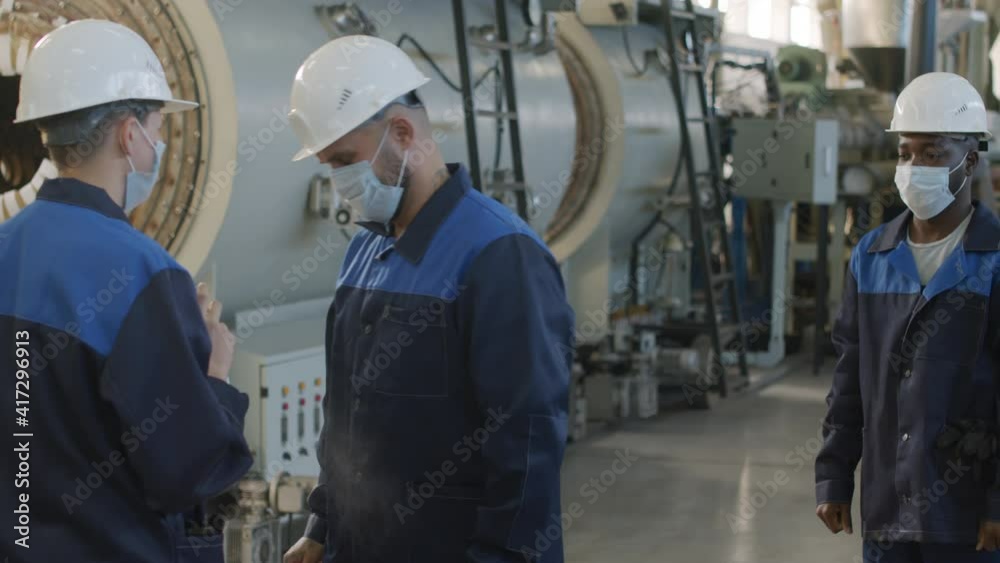 Slowmo medium shot of plant shift supervisor in uniform, face mask and hard hat spraying sanitizer on hands of workers starting their workday Slowmo medium shot of plant shift supervisor in uniform, face mask and hard hat spraying sanitizer on hands of workers starting their workday