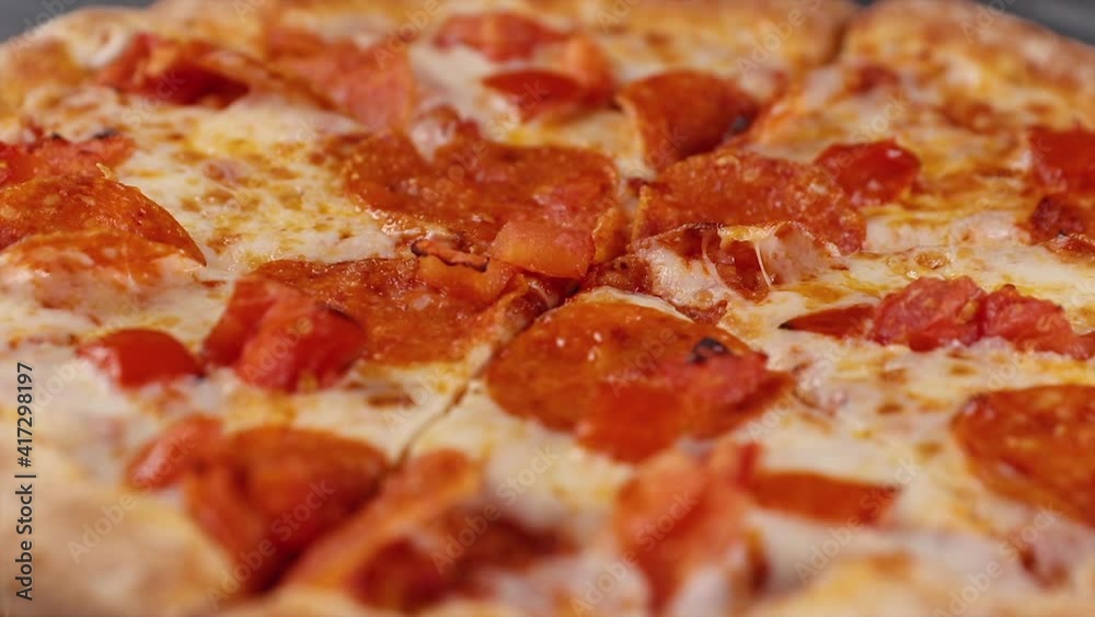whole fresh round pizza with pepperoni and mozzarella cheese rotating on a gray table. tasty fast food background in pizzeria macro view whole fresh round pizza with pepperoni and mozzarella cheese rotating on a gray table. tasty fast food background in pizzeria macro view